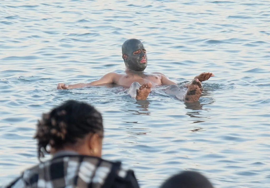 Person swimming in water with mud or clay covering their face and upper body