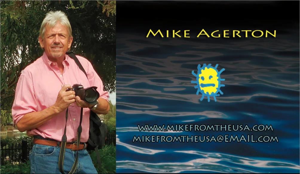Man in pink shirt holding camera standing in front of foliage next to business card design with yellow sun logo and water background