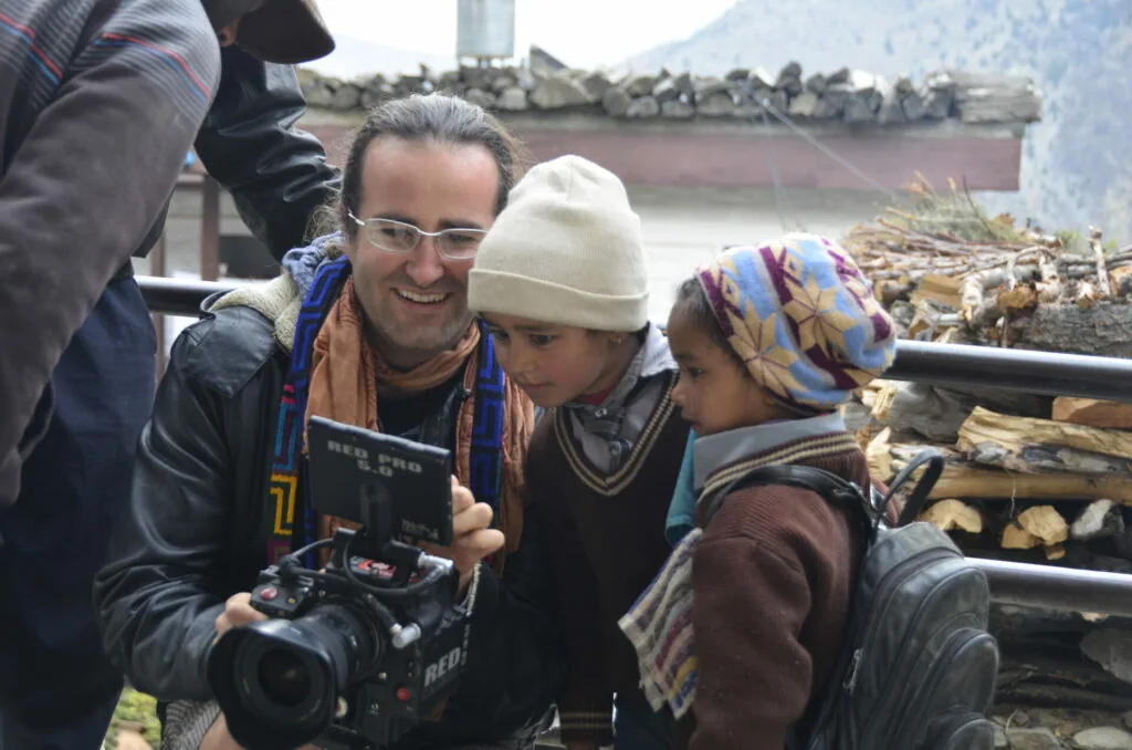 Woman filmmaker with camera showing footage to two children wearing winter hats in mountainous setting