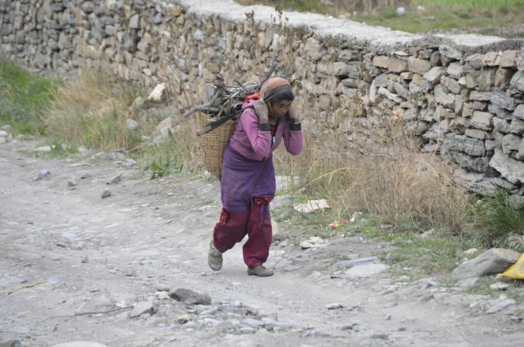 Person carrying woven basket on mountain path near stone wall