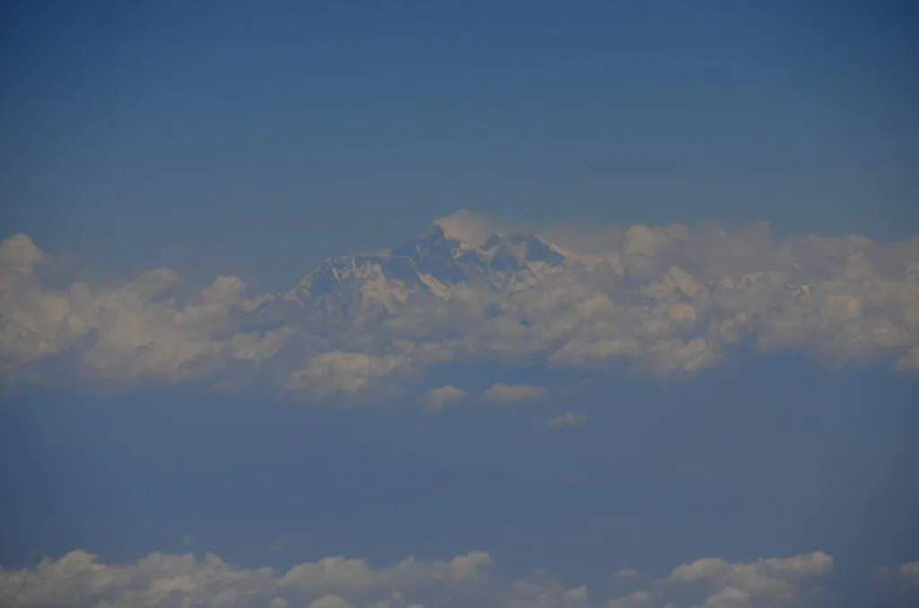 Snow-capped mountain peak rising above white clouds against blue sky