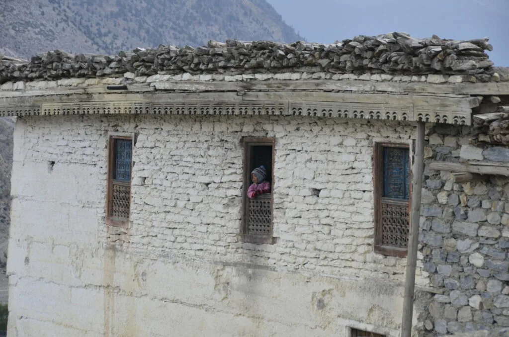 Traditional whitewashed stone building with three wooden-framed windows and decorative roof detail in a mountainous region
