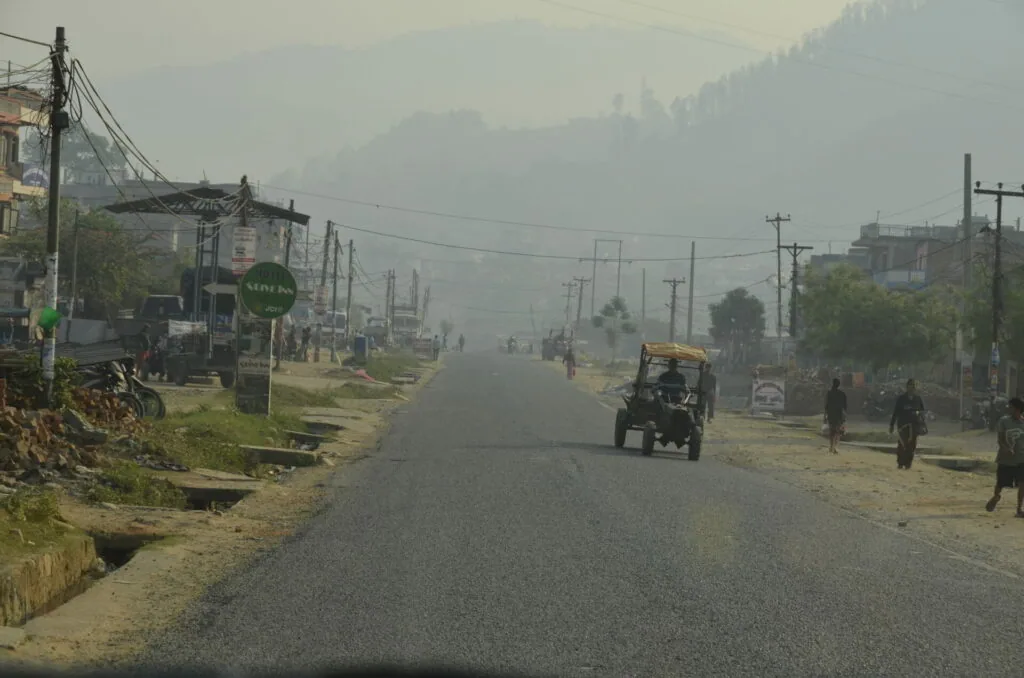 Hazy mountain road with utility poles, buildings, and a yellow truck in rural Nepal