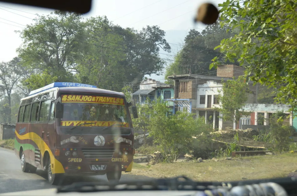 A colorful passenger van with yellow and dark decorative panels parked on a street lined with trees and residential buildings.