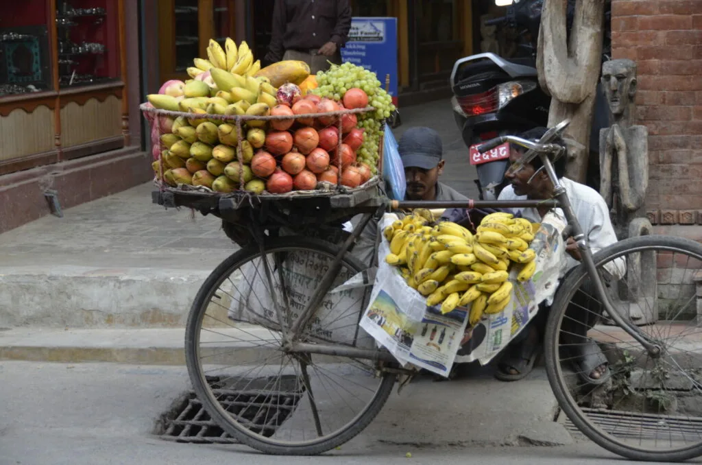 Street vendor with bicycle loaded with bunches of bananas and assorted fruits including apples and oranges