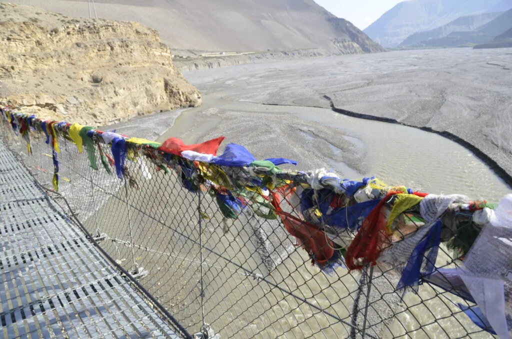 Colorful fabric strips tied to a wire fence overlooking a glacial valley with mountains and a braided river