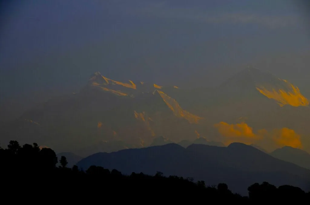 Mountain range silhouette at dusk with golden sunlight illuminating distant peaks against twilight sky