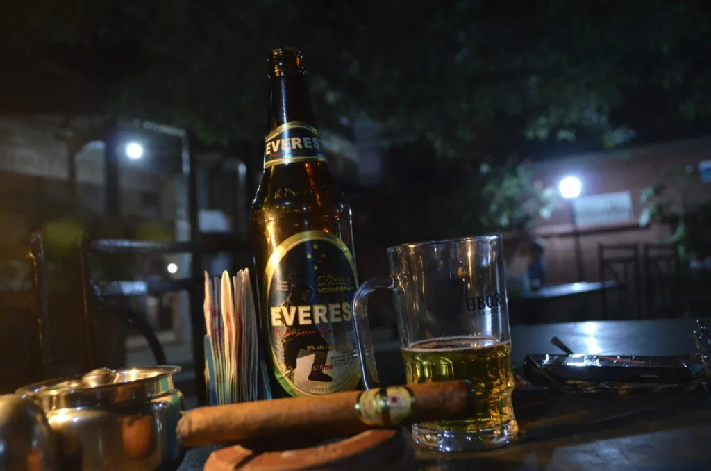 Beer bottle and glass with cigar on nighttime street with blurred buildings in background