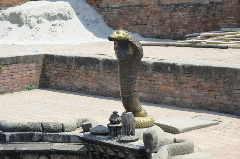 Large cobra statue in an outdoor courtyard with brick walls and stone pavement at a temple or historic site