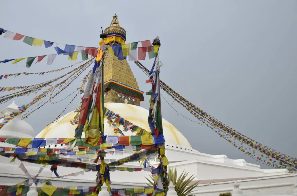 Golden Buddhist stupa with colorful prayer flags strung from the dome and surrounding structures