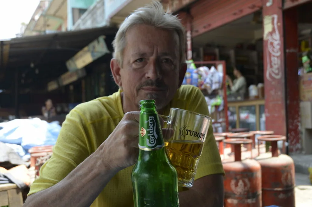 Man in yellow shirt holding green beer bottle and glass at outdoor street market