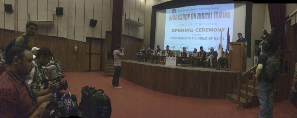Indoor auditorium with audience seated watching opening ceremony for digital filming workshop on projection screen