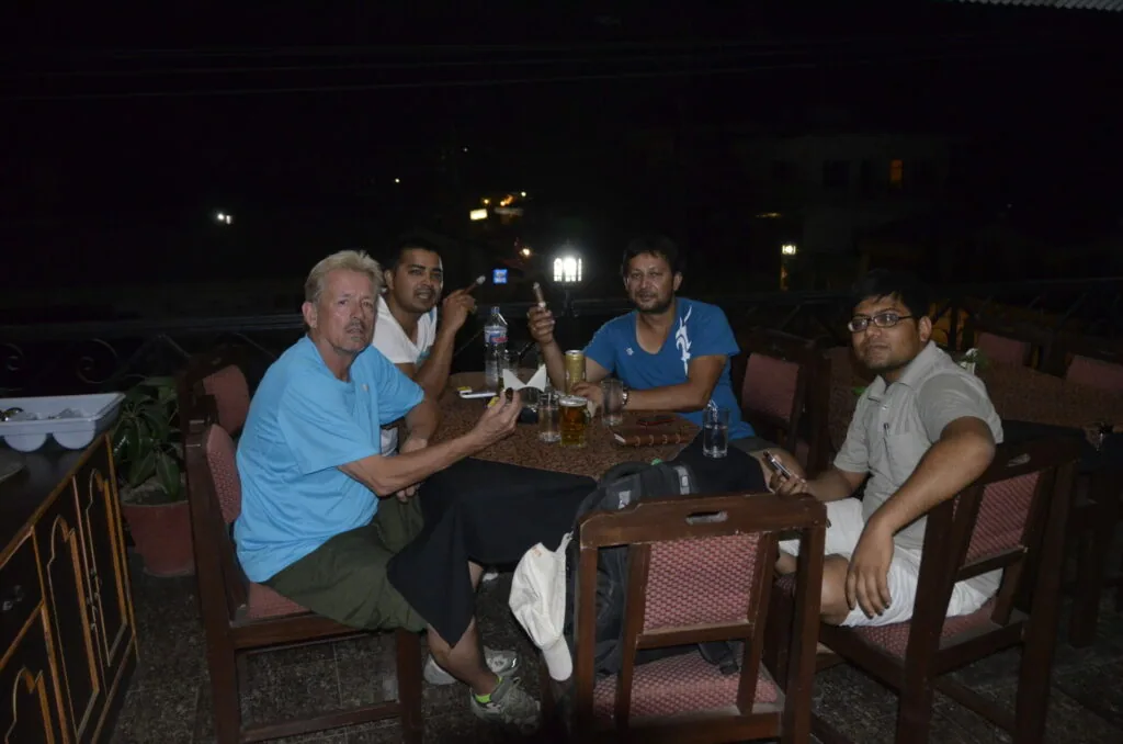 Five men sitting together at an outdoor table at night with drinks and food