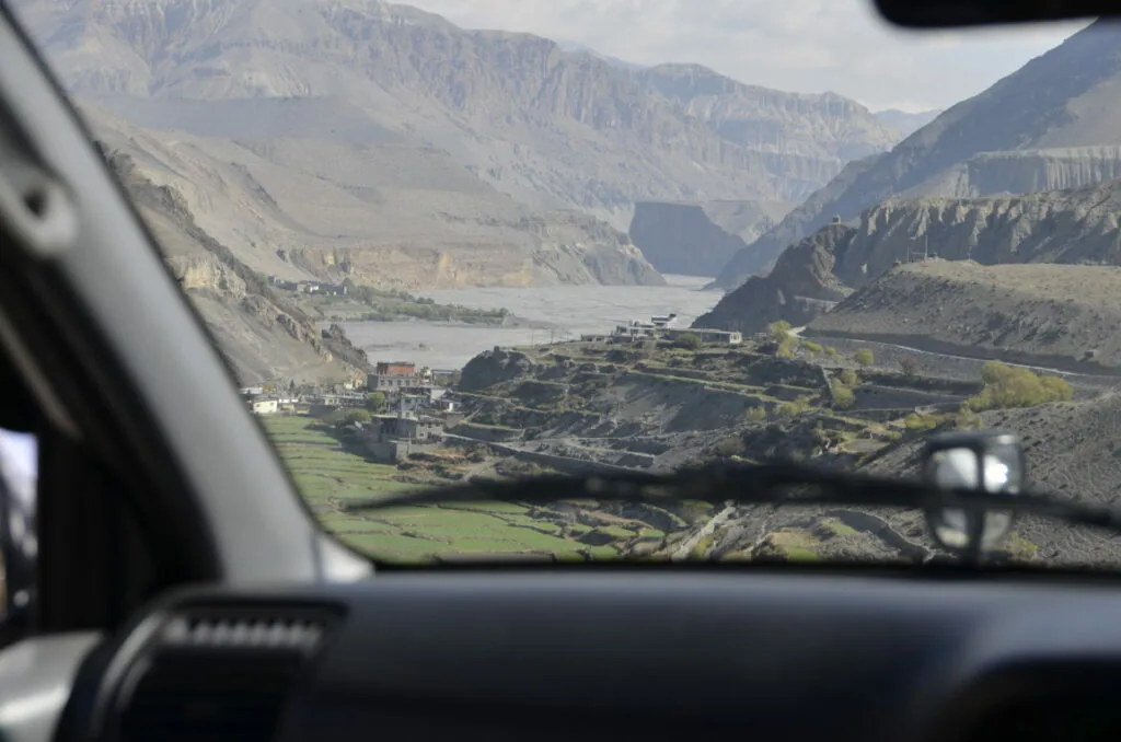 View through car window of mountain valley with river, terraced fields, and settlements nestled between steep rocky peaks