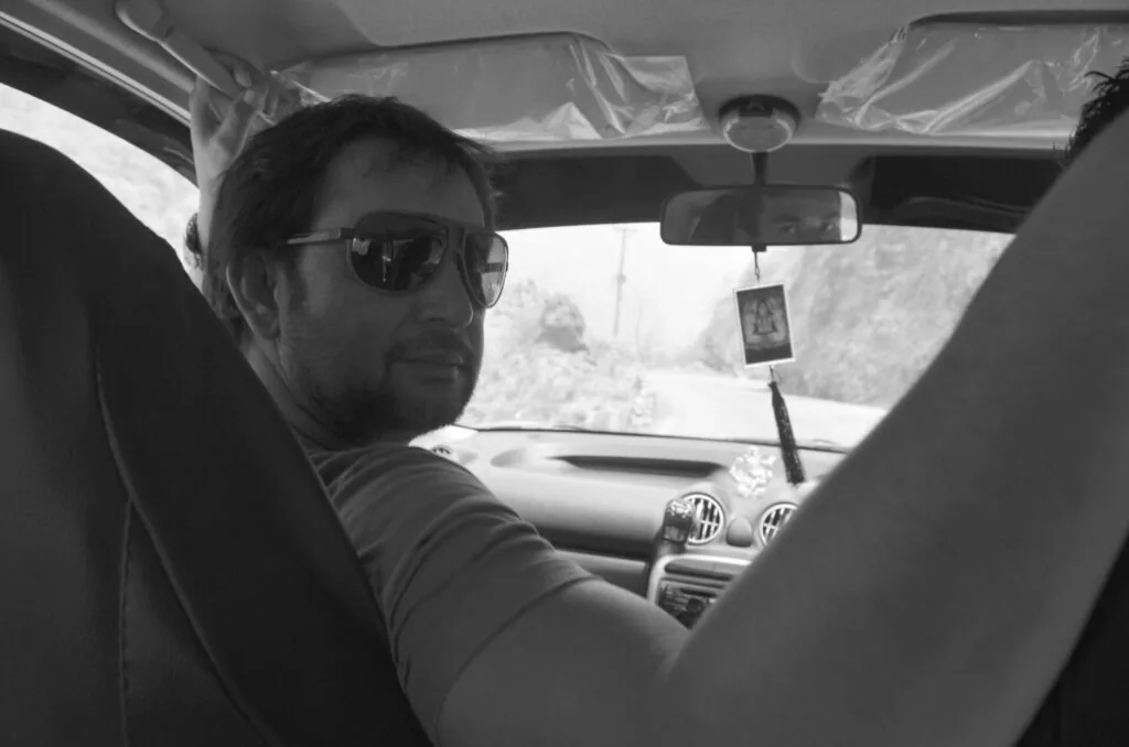 Man wearing sunglasses sitting in driver's seat of car with snowy landscape visible through windshield