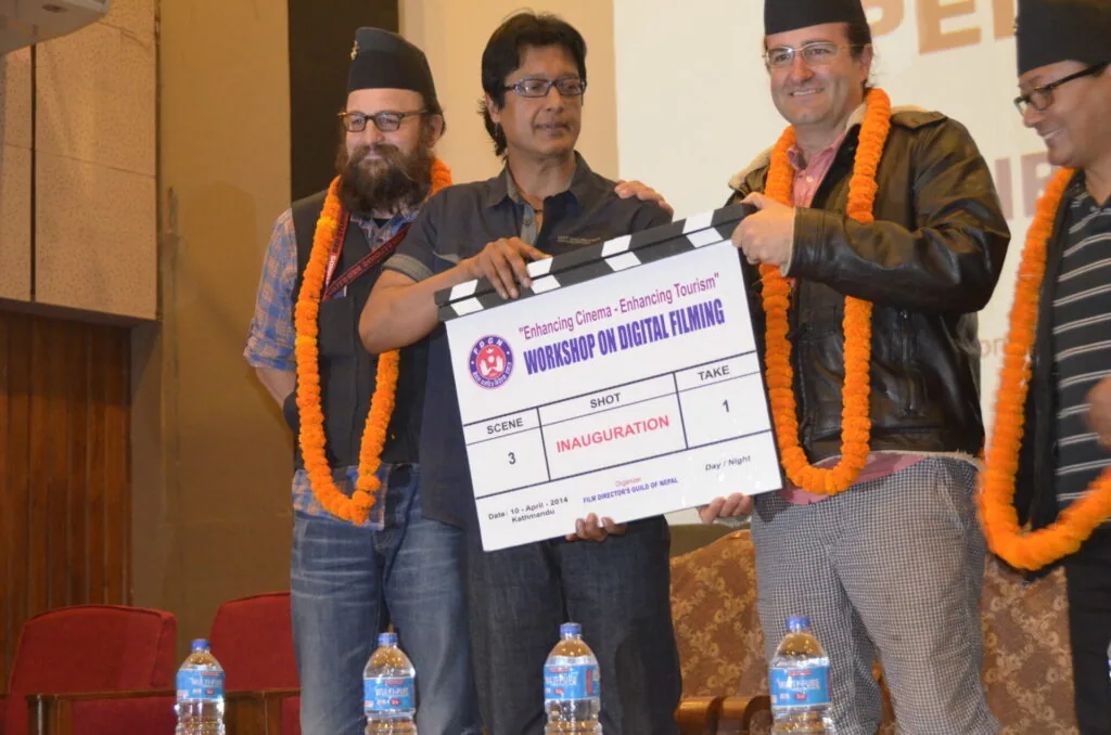 Four men wearing orange garlands hold a film clapperboard at a workshop inauguration event