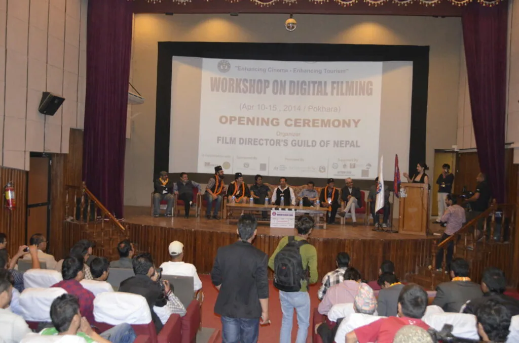 Opening ceremony of a workshop on digital filming organized by the Film Director's Guild of Nepal, with panelists seated on stage and audience members seated in an auditorium.