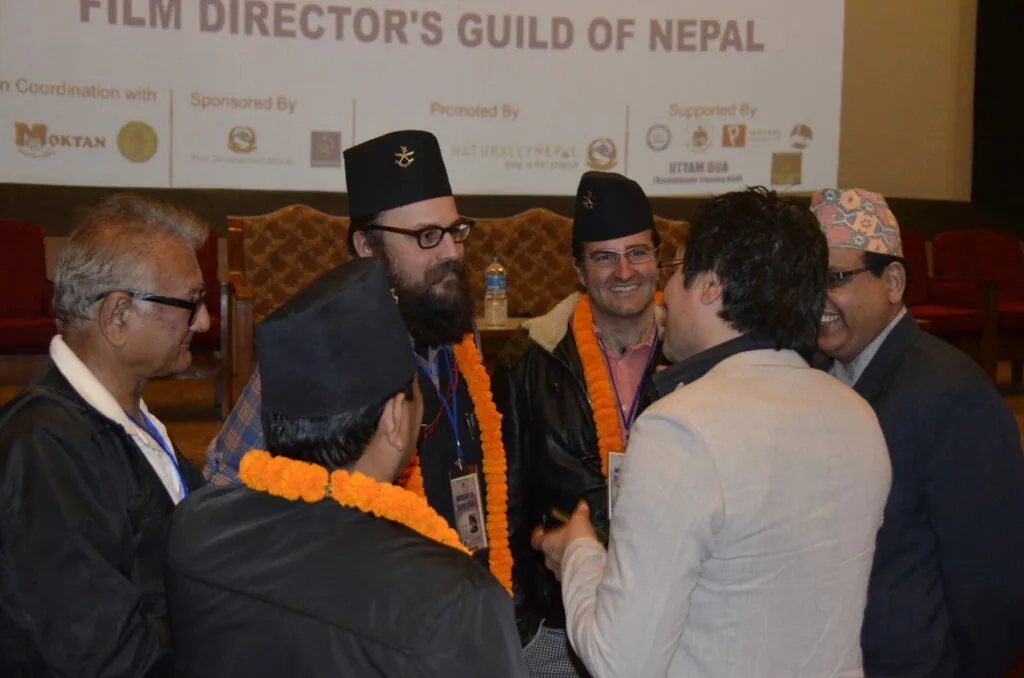 Group of men in formal attire and traditional Nepali hats conversing at Film Director's Guild of Nepal event