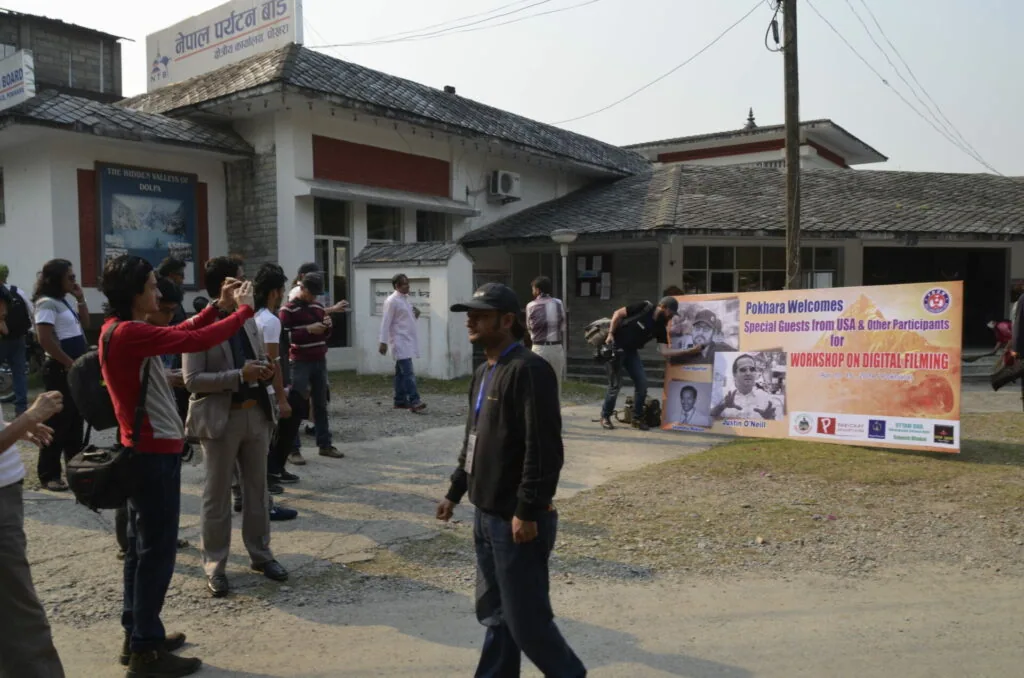 Outdoor gathering with people standing in a courtyard near buildings with a welcome banner for a digital filming workshop