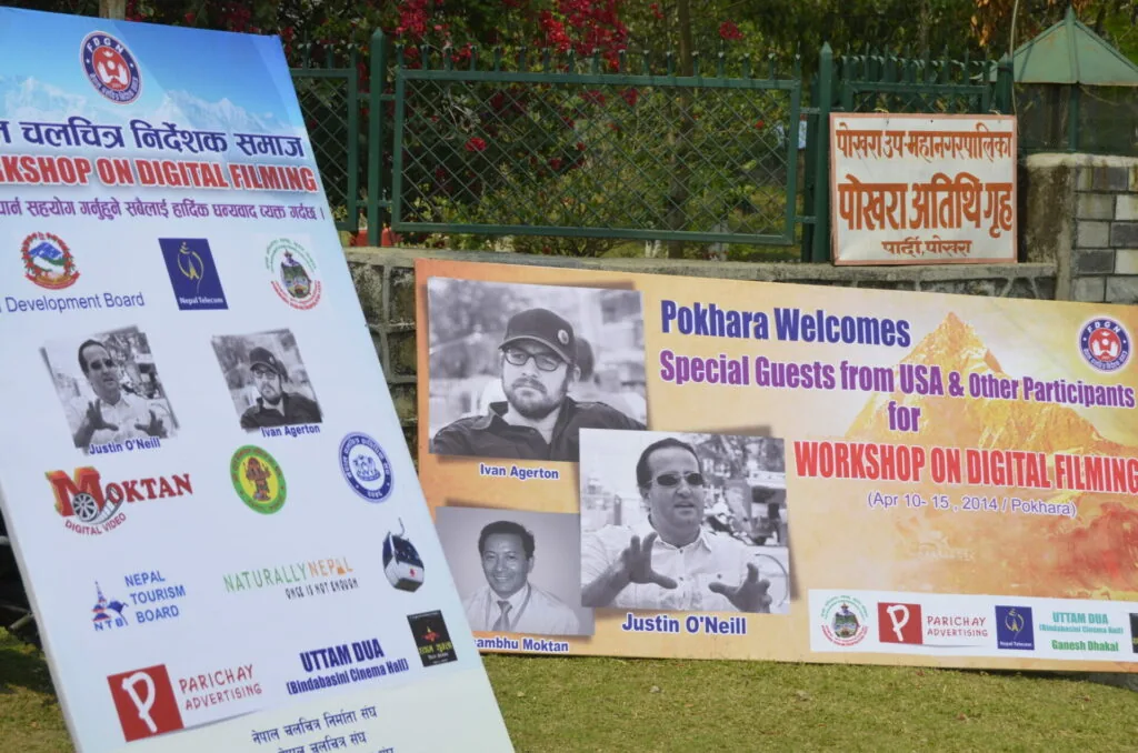 Outdoor event banners advertising a workshop on digital filming in Pokhara, Nepal, with sponsor logos and photos of guest speakers.