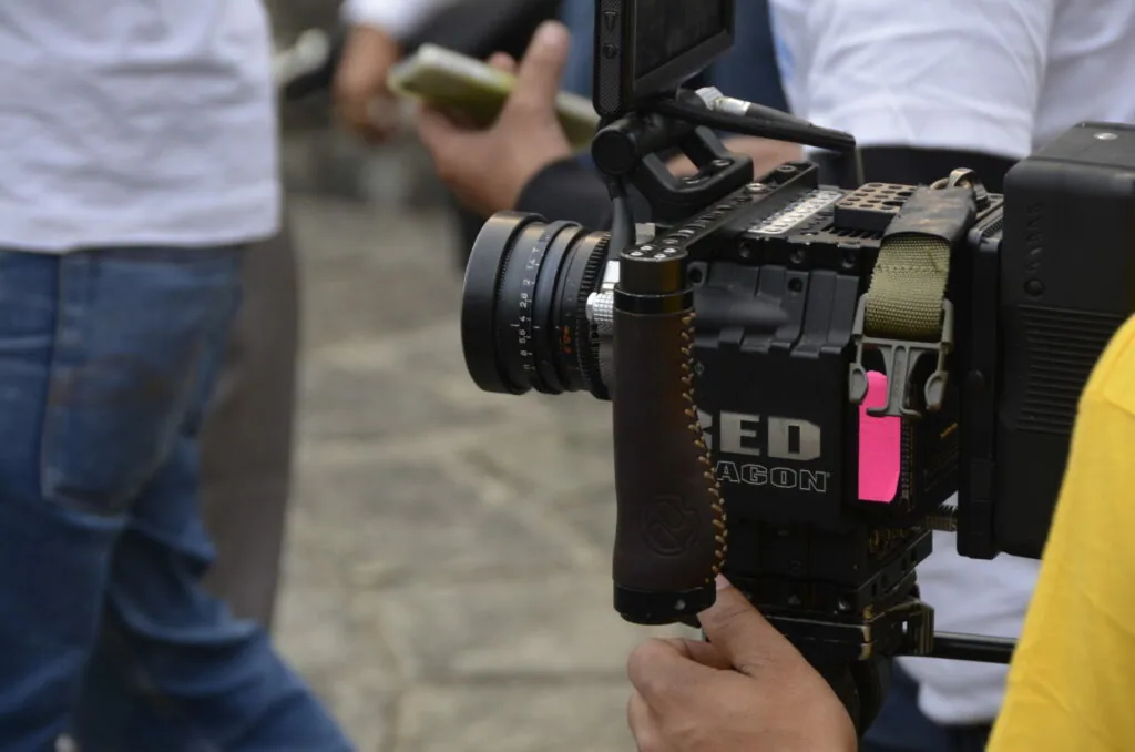 Professional cinema camera with lens held during outdoor filming production with crew members visible in background