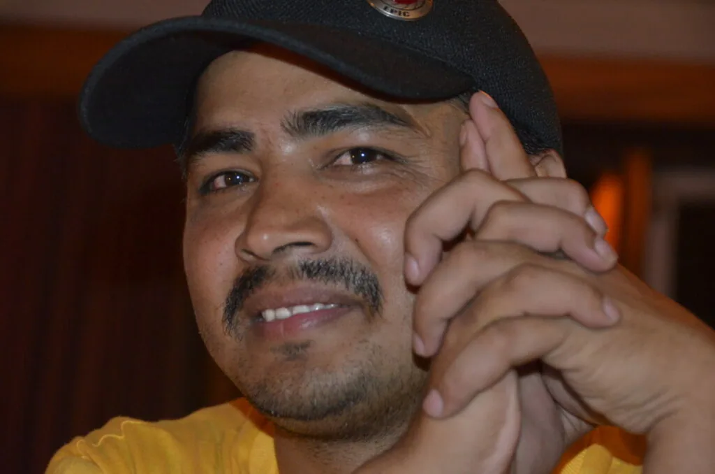 Man wearing black cap and yellow shirt giving thumbs up gesture indoors