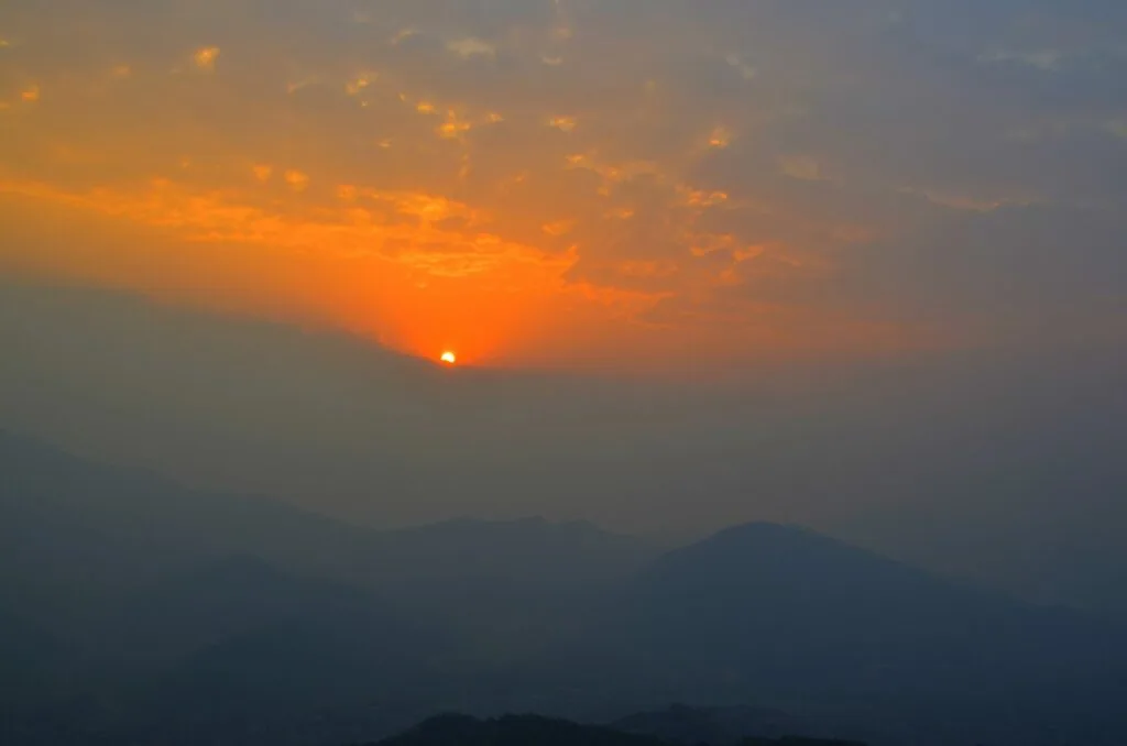 Sun setting over mountain silhouettes with orange and golden sky at dusk