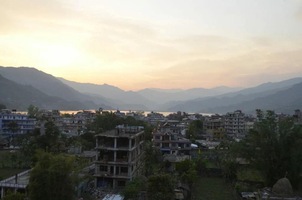 Mountain valley at sunset with buildings and a lake nestled between forested hillsides at dusk