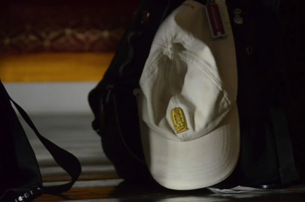White baseball cap with gold rectangular patch on display with dark fabric backdrop