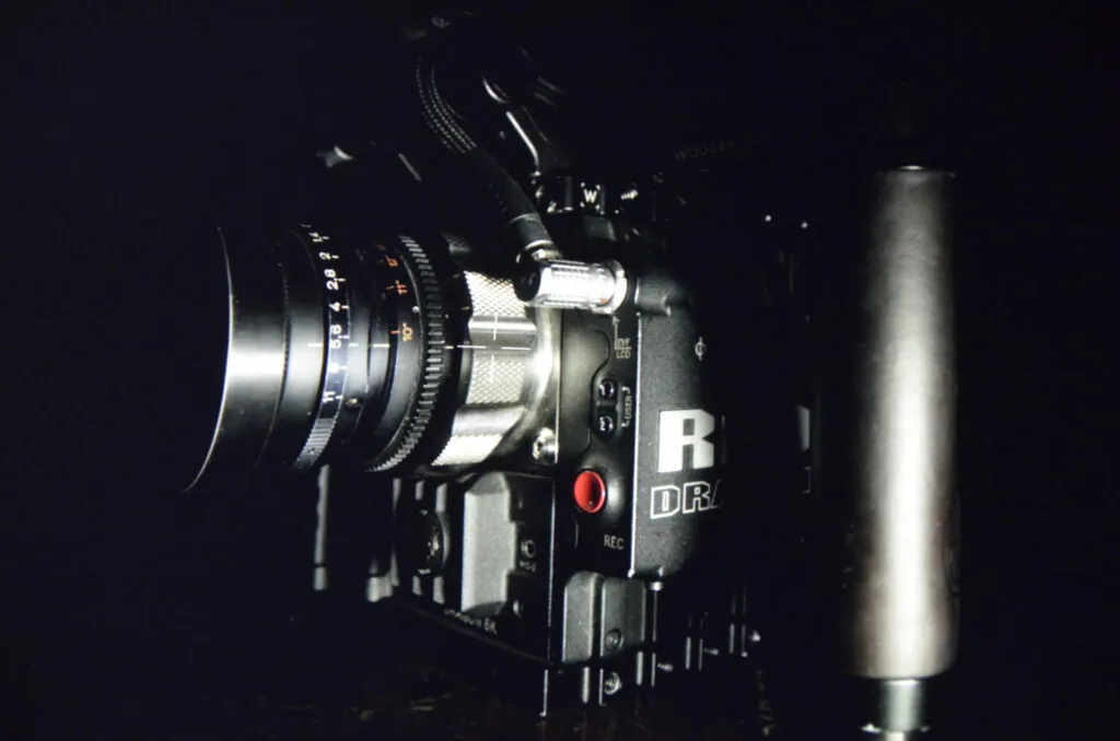Professional cinema camera with lens mounted on left side and cylindrical microphone on right side against dark background