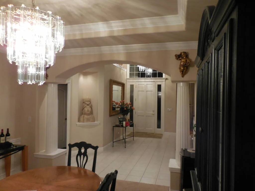 Elegant foyer with crystal chandelier, arched ceiling, white tile flooring, and classical decor including a bust sculpture and decorative gold wall accent