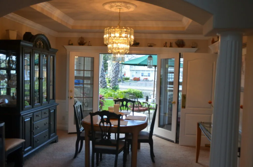 Formal dining room with round wood table, black chairs, crystal chandelier, and glass doors opening to outdoor patio