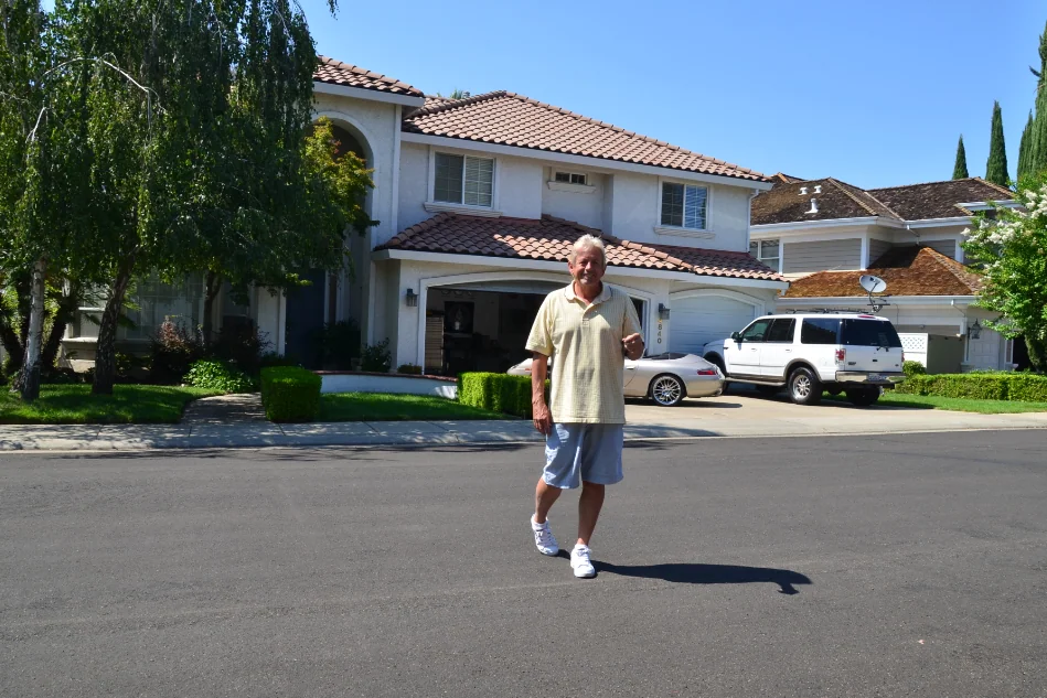 Man standing in street in front of two-story white house with tile roof and driveway