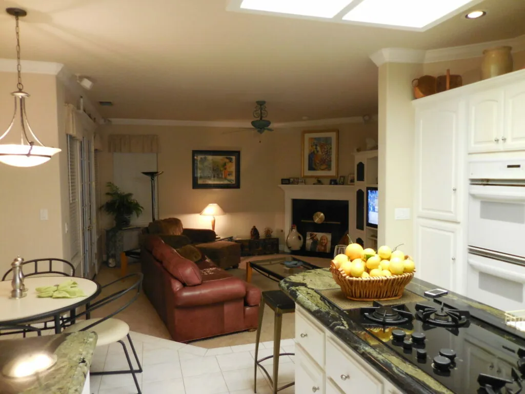Open-concept kitchen and living room with white cabinetry, granite countertops, gas range, red leather chair, fireplace, and pendant lighting