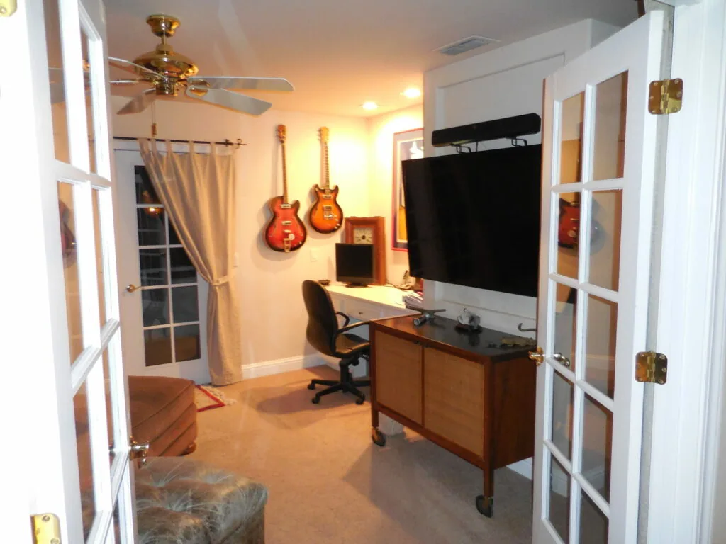 Home office and music room with desk, monitor, guitars on wall, and ceiling fan