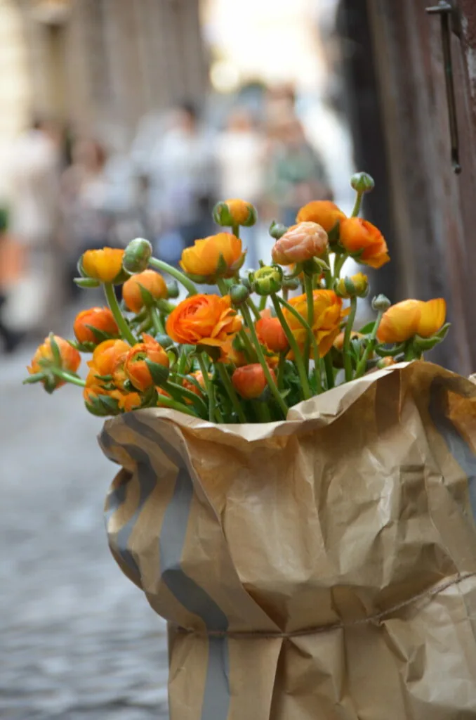 Orange and yellow ranunculus flowers in a paper bag on a blurred street