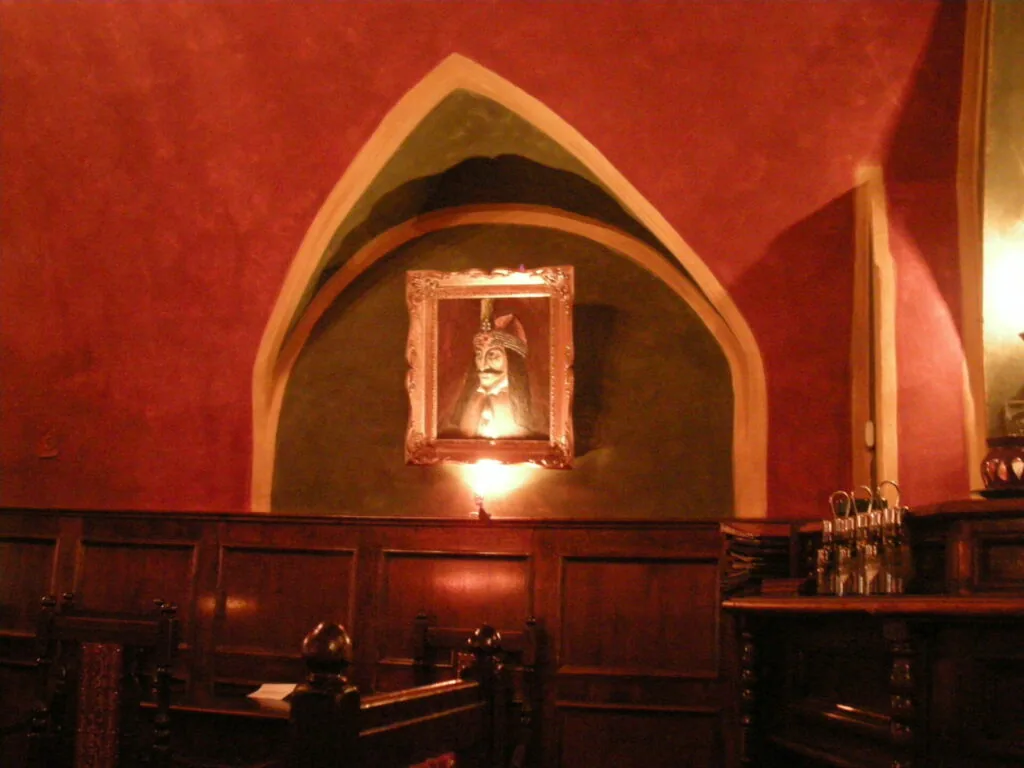 Gothic interior with red walls, pointed arch alcove, framed portrait, dark wood paneling, and decorative sconces.
