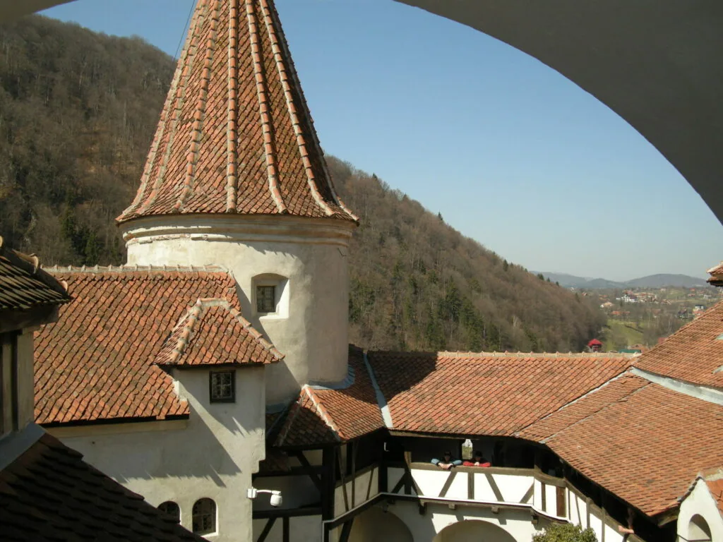 Medieval castle tower with conical roof and terracotta tiles overlooking forested valley and mountains