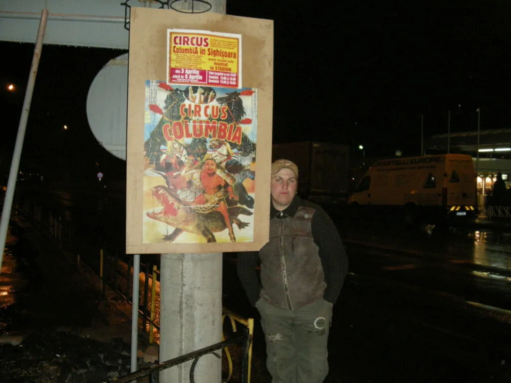 Person standing next to vintage Circus Columbia poster on wooden display board at night