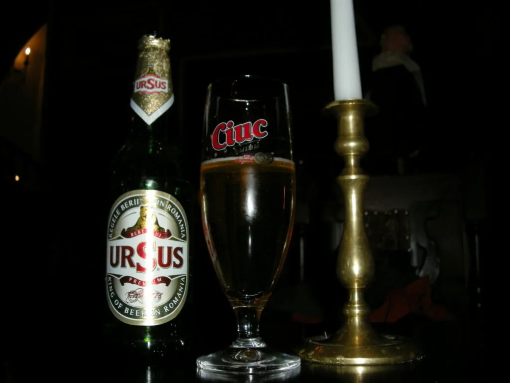 Beer bottle with label next to a glass of dark beer and brass candlestick on dark background