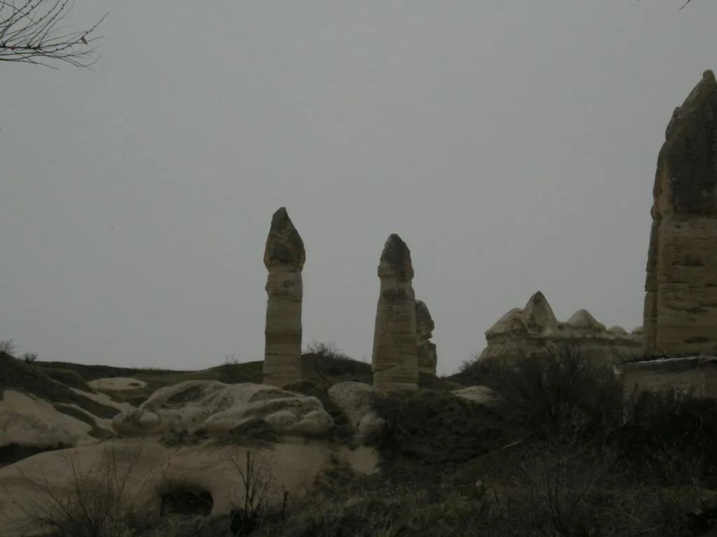 Tall stone rock formations with pointed tops rising from desert landscape under overcast sky