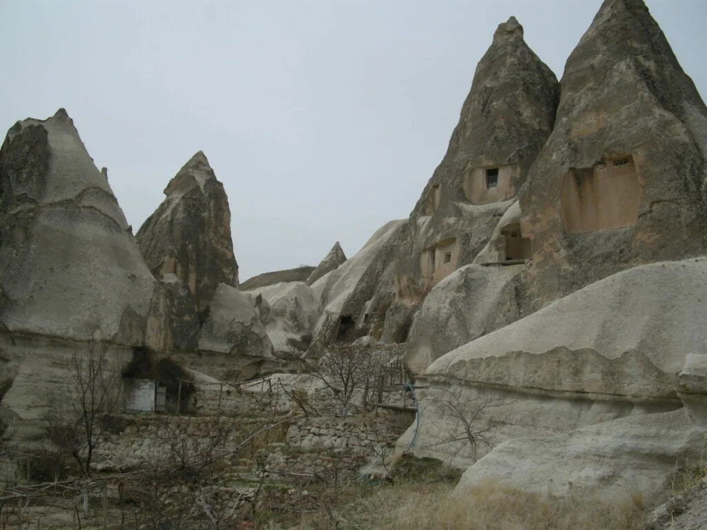 Ancient cave dwellings carved into tall rock formations with fairy chimney structures