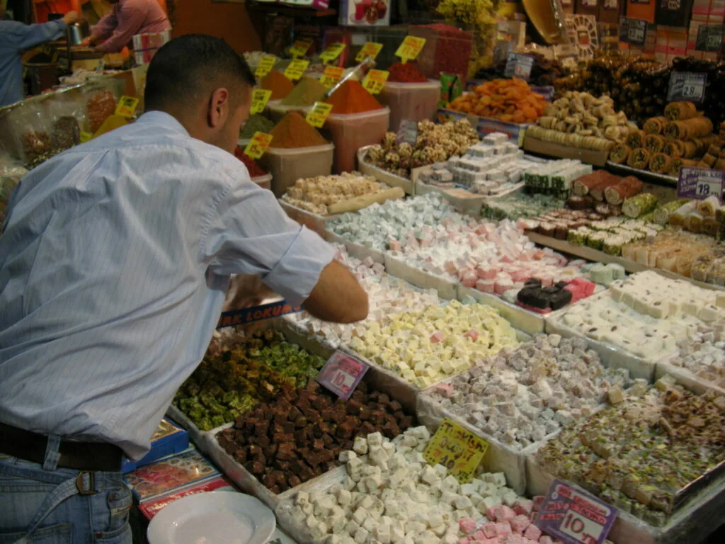 Man in light blue shirt examining display of colorful candies and sweets at market stall with yellow price tags