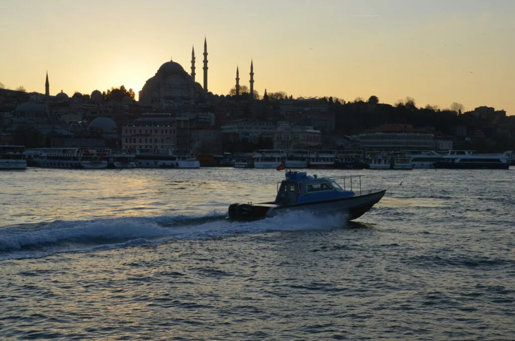 Blue police boat in water at sunset with mosque and city skyline silhouetted against golden sky