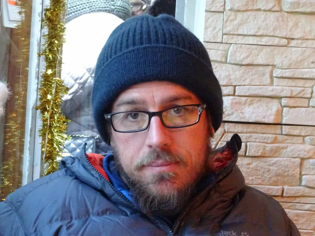 Man wearing dark beanie hat and glasses with beard, dressed in dark winter jacket