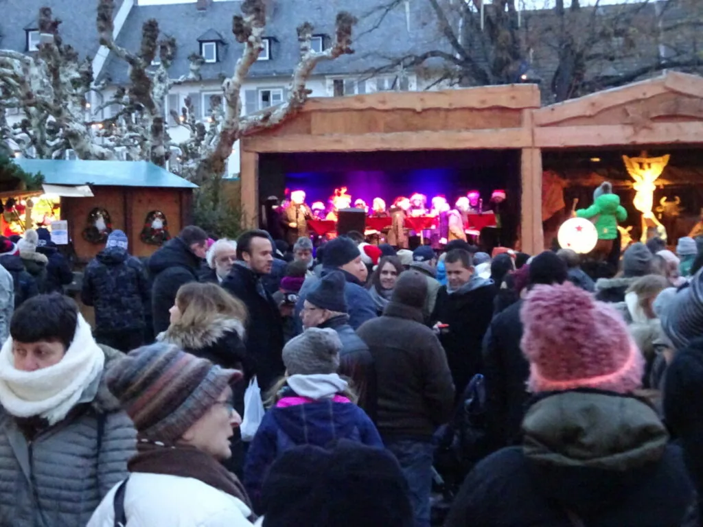 Outdoor winter festival crowd watching performers on illuminated stage with buildings and bare tree in background