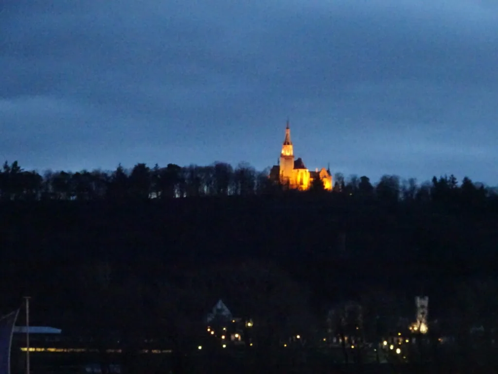Illuminated castle on hilltop at dusk with forested silhouette and village lights below