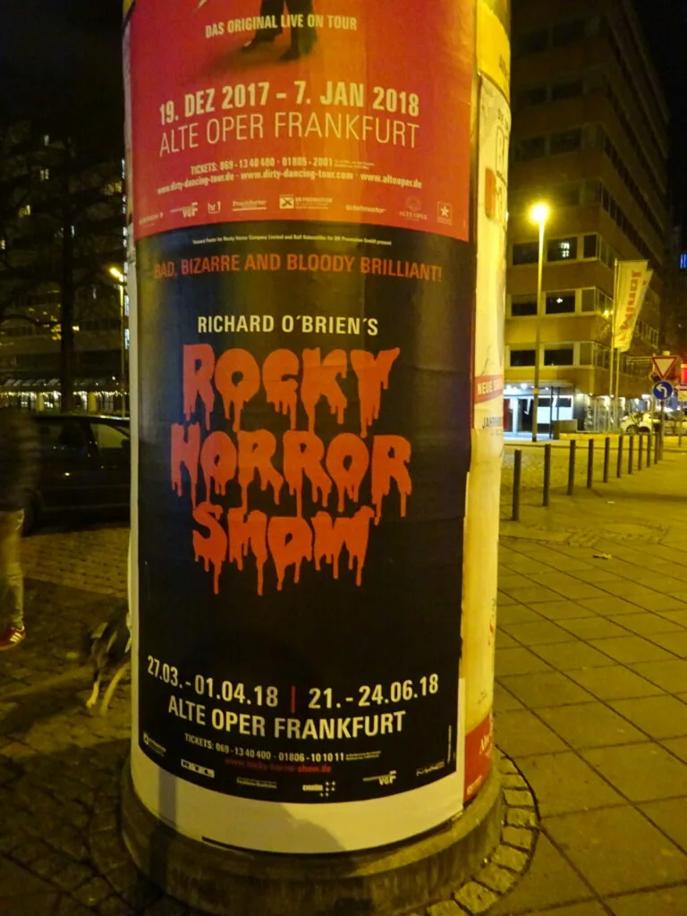 Theater advertisement posters on cylindrical column at night, showing Rocky Horror Show and other productions at Alte Oper Frankfurt
