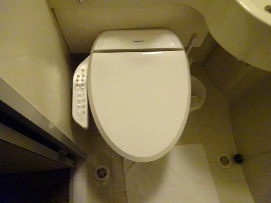 White electronic toilet seat with control panel on side in beige bathroom