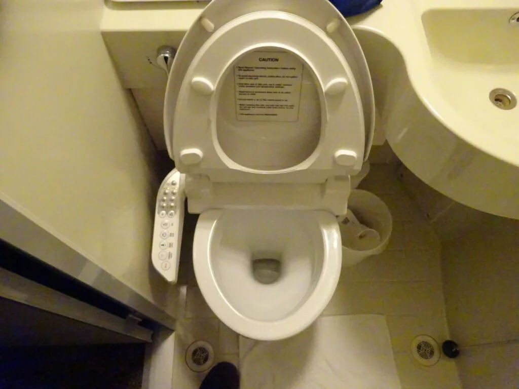 White toilet with bidet seat and control panel in beige bathroom with sink visible